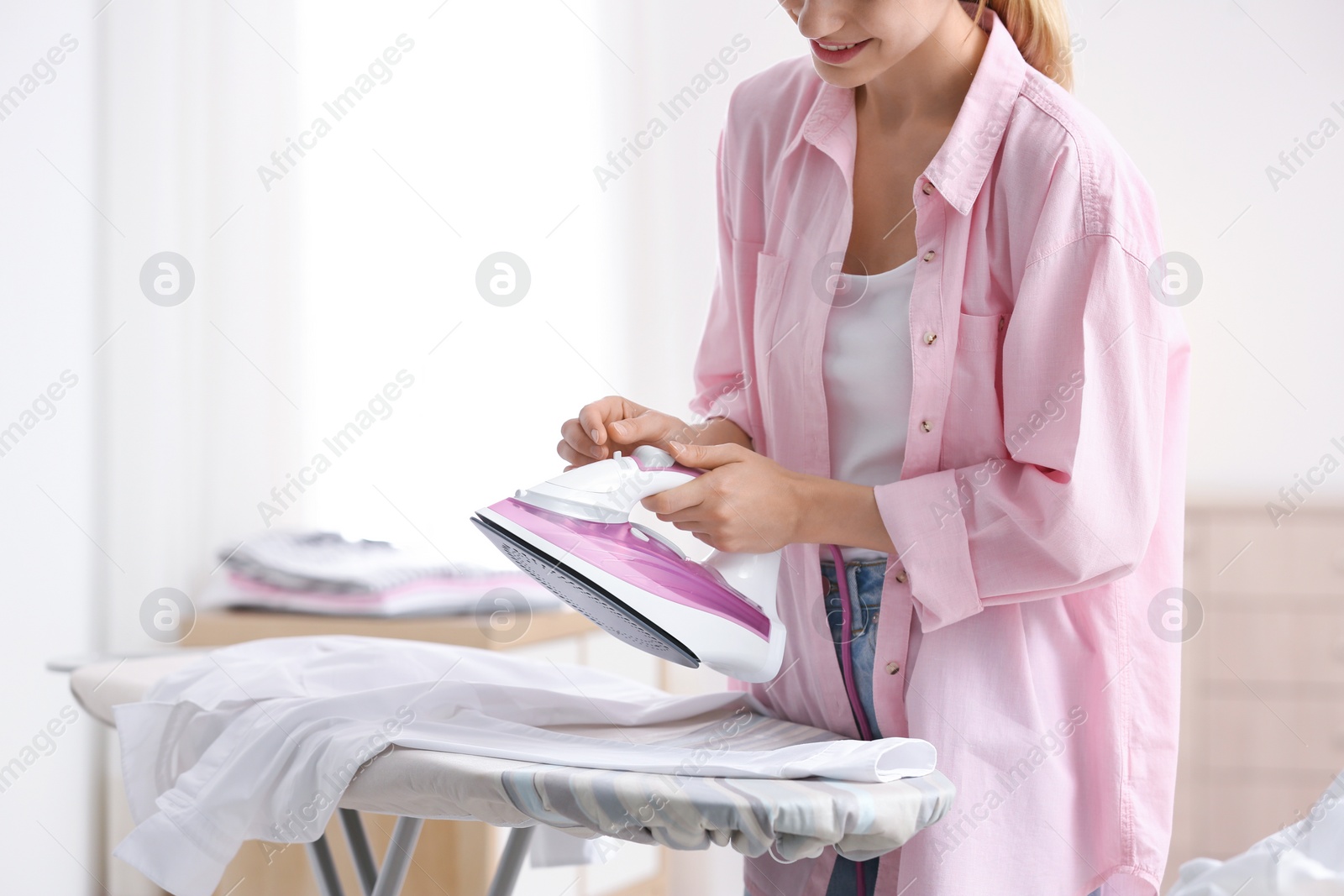 Photo of Young woman ironing clean laundry on board indoors, closeup