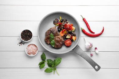 Tasty fried steak with vegetables in pan and ingredients on white wooden table, flat lay