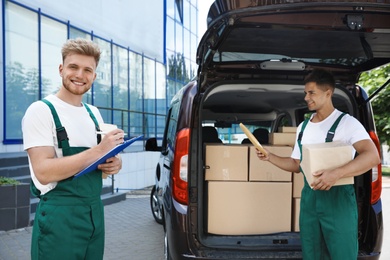Photo of Young couriers with parcels near delivery car outdoors