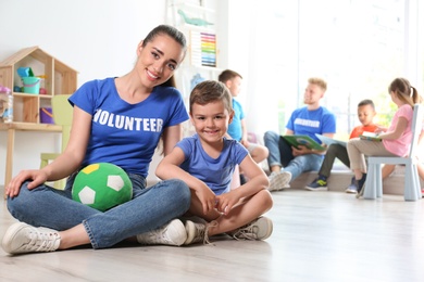 Young female volunteer with little boy sitting on floor indoors