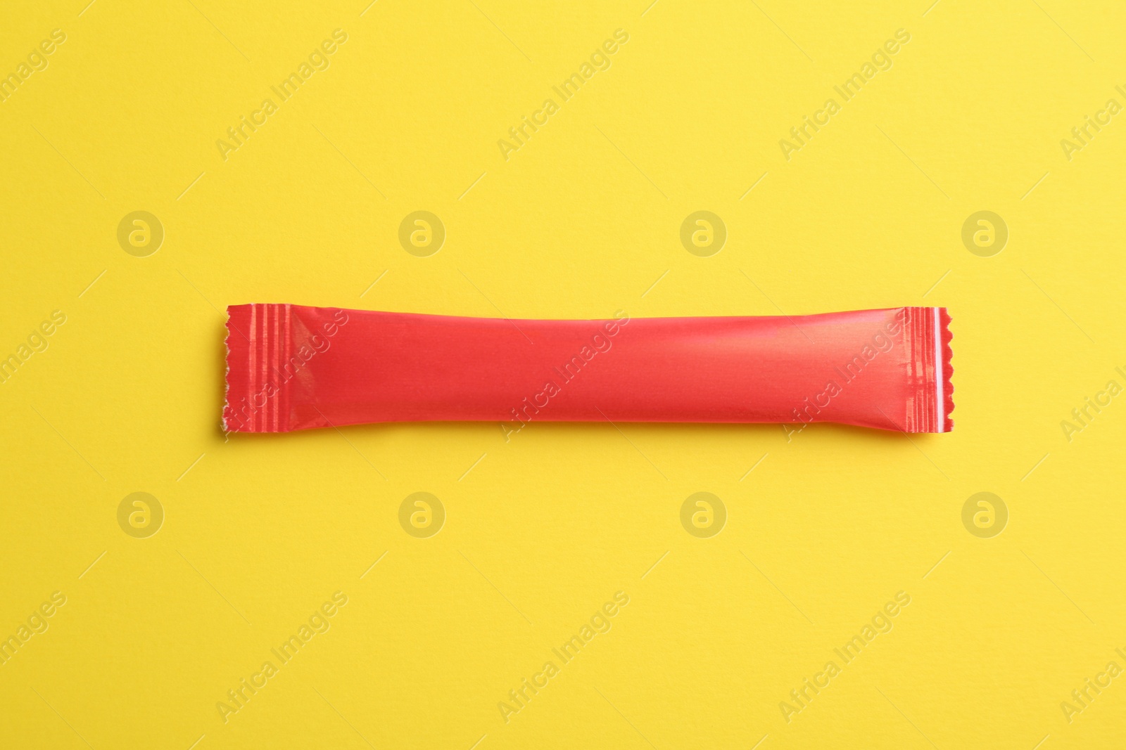 Photo of Red stick of sugar on yellow background, top view