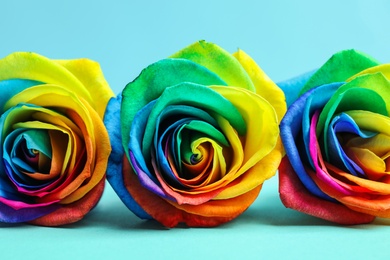 Photo of Rainbow rose flowers on table against color background