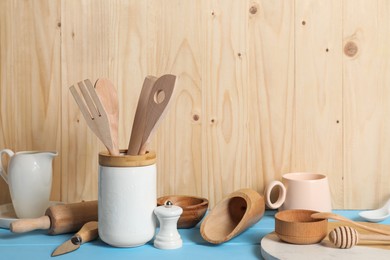 Photo of Set of different kitchen utensils on light blue table against wooden background, space for text