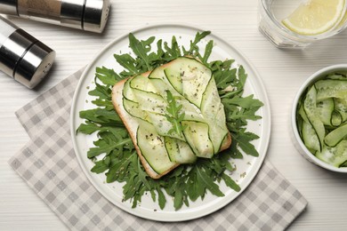 Photo of Tasty cucumber sandwich with seasoning and arugula on white wooden table, flat lay