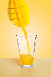 Image of Making mango fresh. Juice pouring from mango into glass on pale yellow background