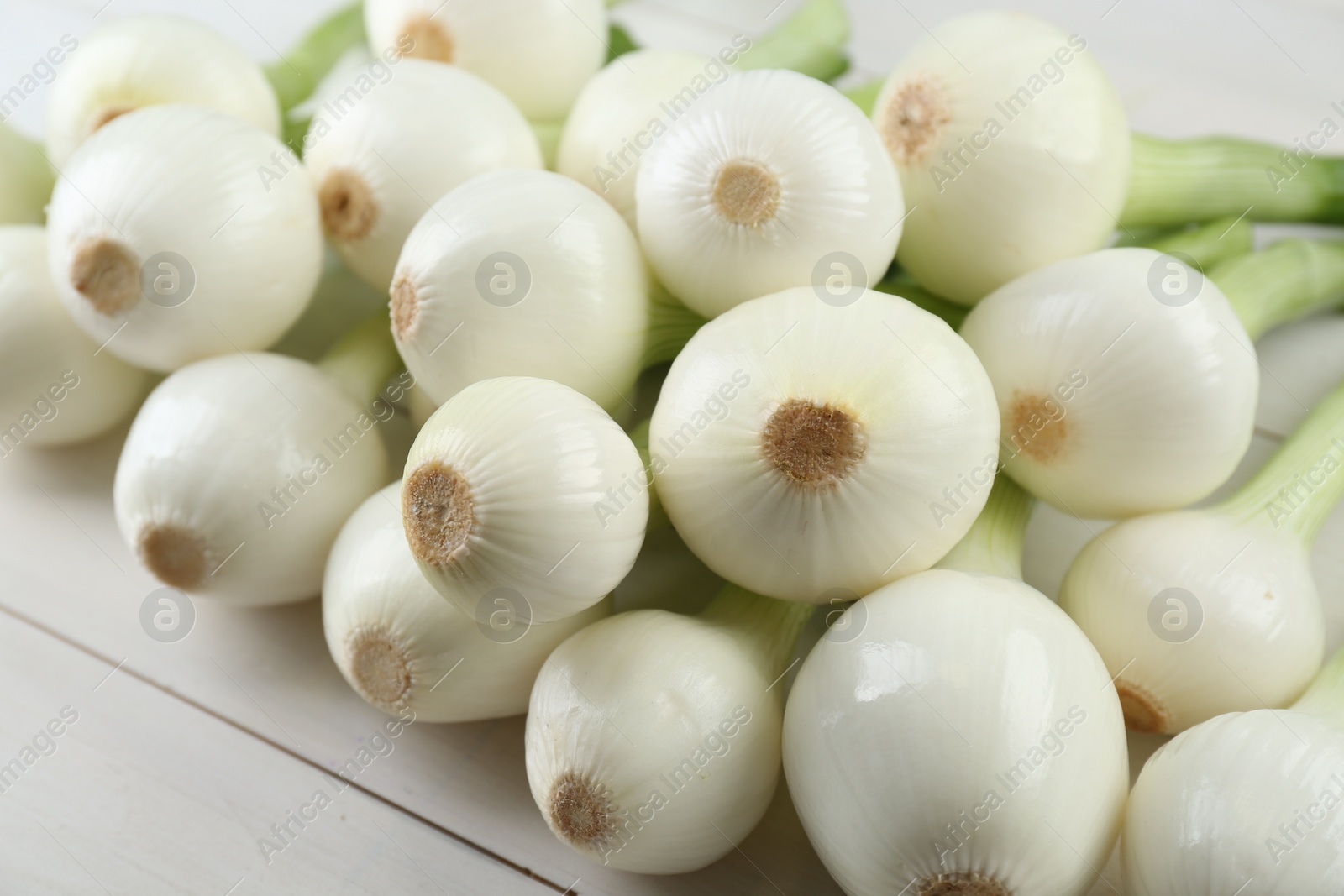 Photo of Whole green spring onions on white wooden table, closeup