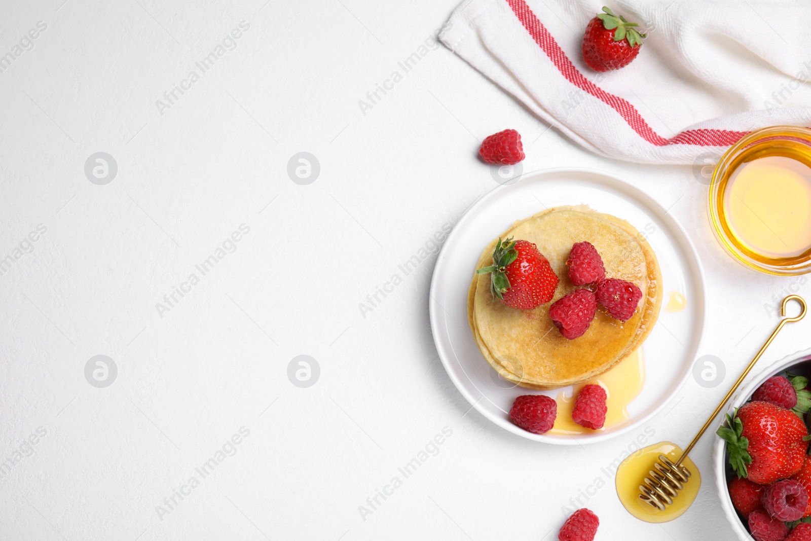 Photo of Tasty pancakes served with fresh berries and honey on white table, flat lay. Space for text