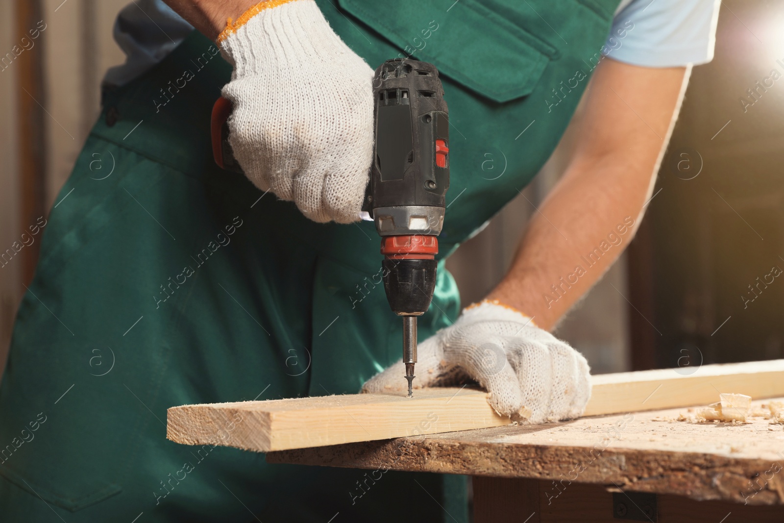 Photo of Professional carpenter twisting screw into wooden plank with drill in workshop, closeup