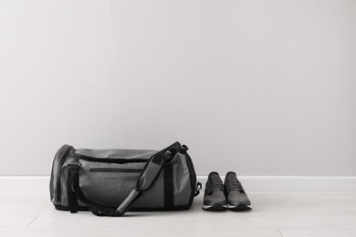 Photo of Grey sports bag and sneakers on floor near light wall, space for text