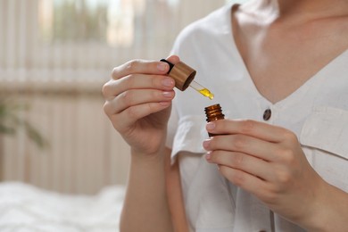 Young woman with bottle of essential oil indoors, closeup. Space for text