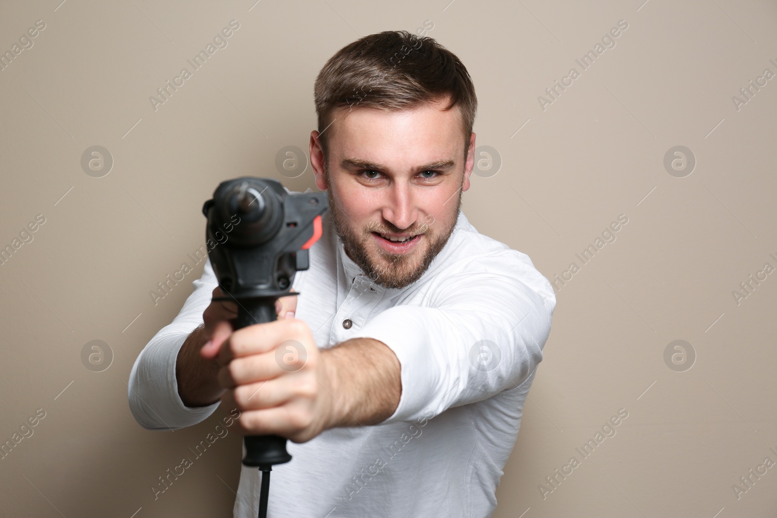 Photo of Young working man with rotary hammer on beige background