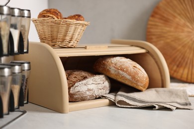 Photo of Wooden bread basket, freshly baked loaves and croissants on white marble table in kitchen