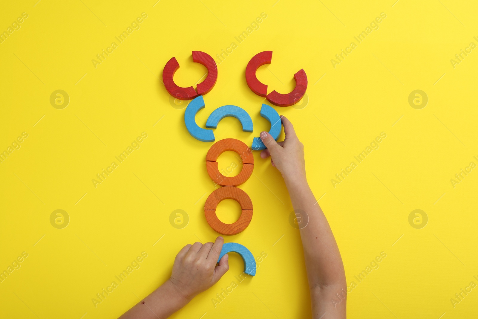 Photo of Motor skills development. Boy playing with colorful wooden arcs at yellow table, top view