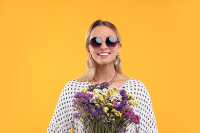 Photo of Portrait of smiling hippie woman with bouquet of flowers on yellow background