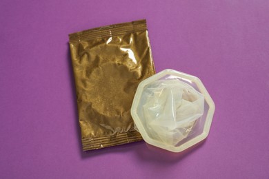 Unpacked female condom and package on violet background, above view. Safe sex