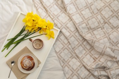 Bouquet of beautiful daffodils, bun and coffee on bed, top view. Space for text