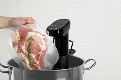 Photo of Woman putting vacuum packed meat into pot with sous vide cooker, closeup and space for text. Thermal immersion circulator