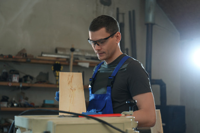 Photo of Professional carpenter with wooden board in workshop