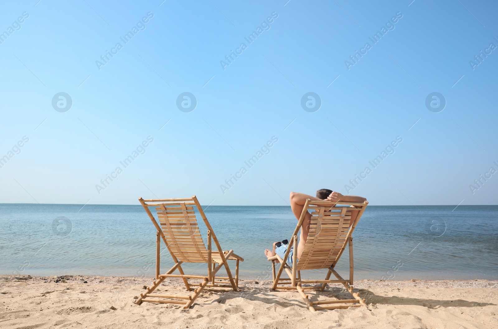 Photo of Young man relaxing in deck chair on sandy beach