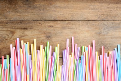 Photo of Colorful plastic drinking straws on wooden table, flat lay. Space for text