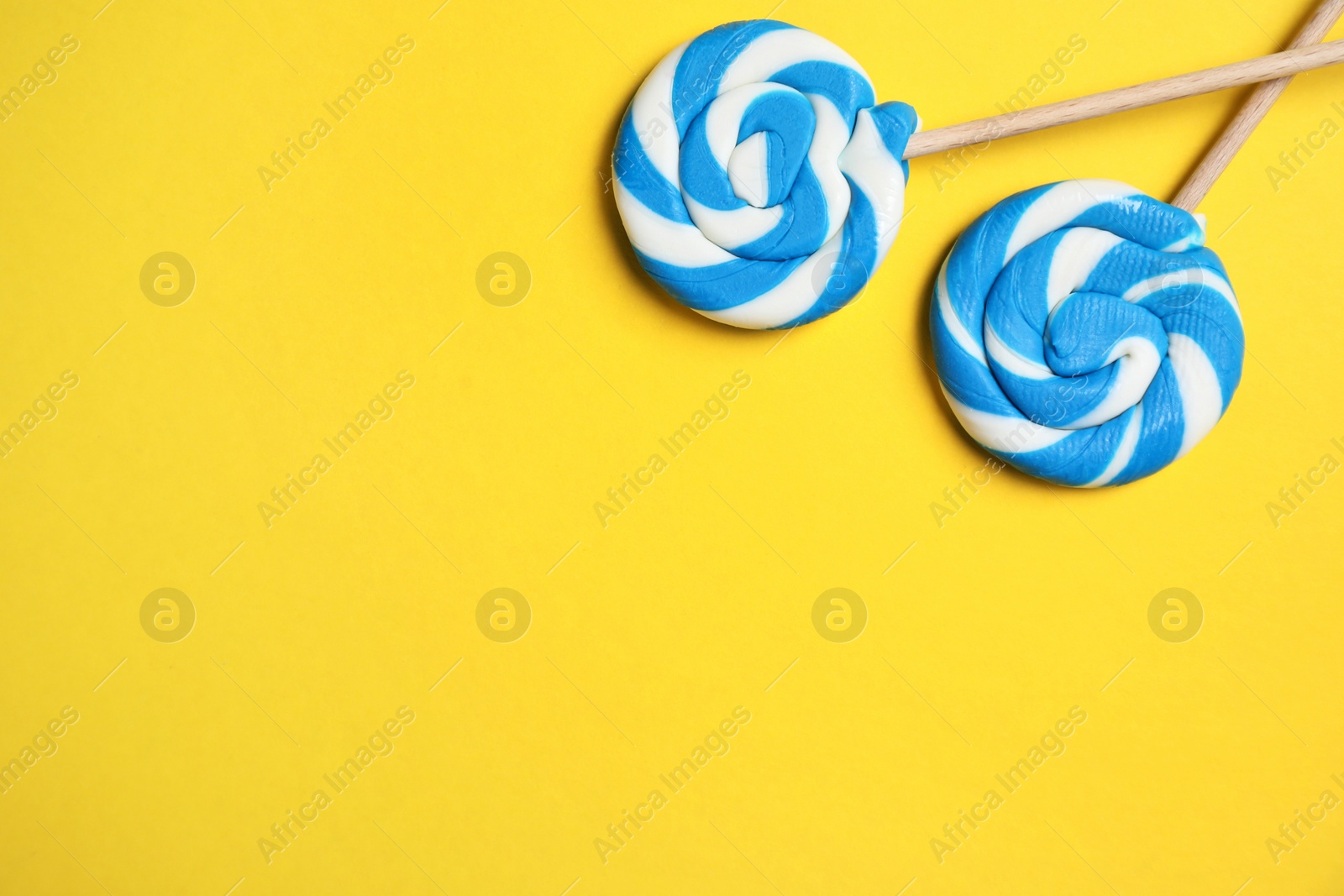 Photo of Sticks with bright lollipops on yellow background, flat lay. Space for text