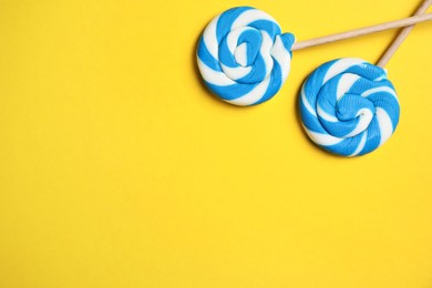 Photo of Sticks with bright lollipops on yellow background, flat lay. Space for text