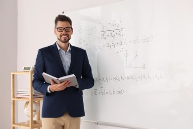 Happy teacher with book at whiteboard in classroom during math lesson
