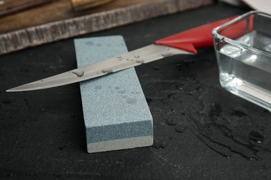 Photo of Sharpening stone, knife and water on black table, closeup