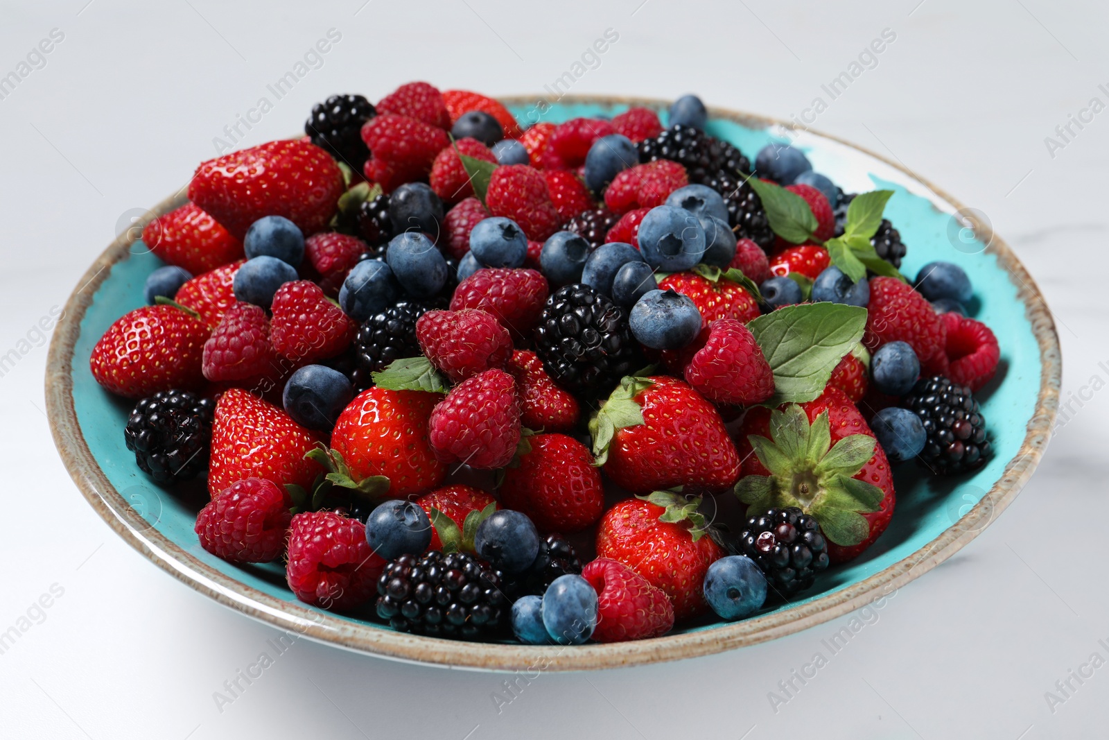 Many different fresh ripe berries in bowl on white table, closeup Photo of Many different fresh ripe berries in bowl on white table, closeup
