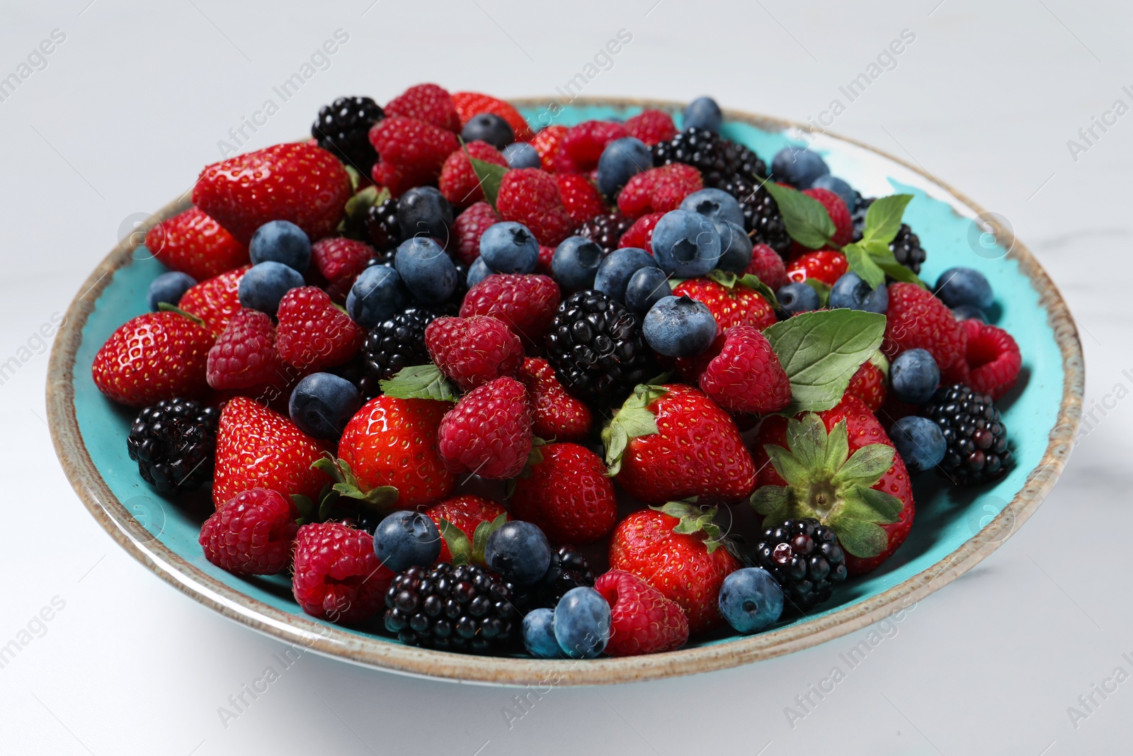 Photo of Many different fresh ripe berries in bowl on white table, closeup