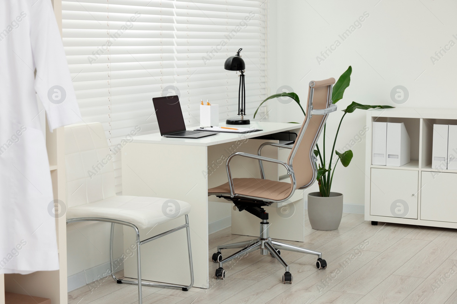 Photo of Doctor's workplace. Chairs, laptop and clipboard on white table in clinic