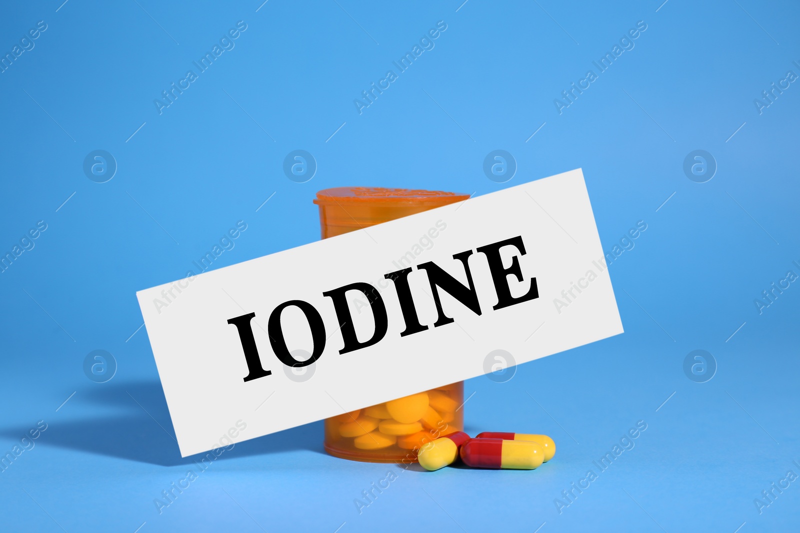 Photo of Paper note with word Iodine, bottle and pills on light blue background