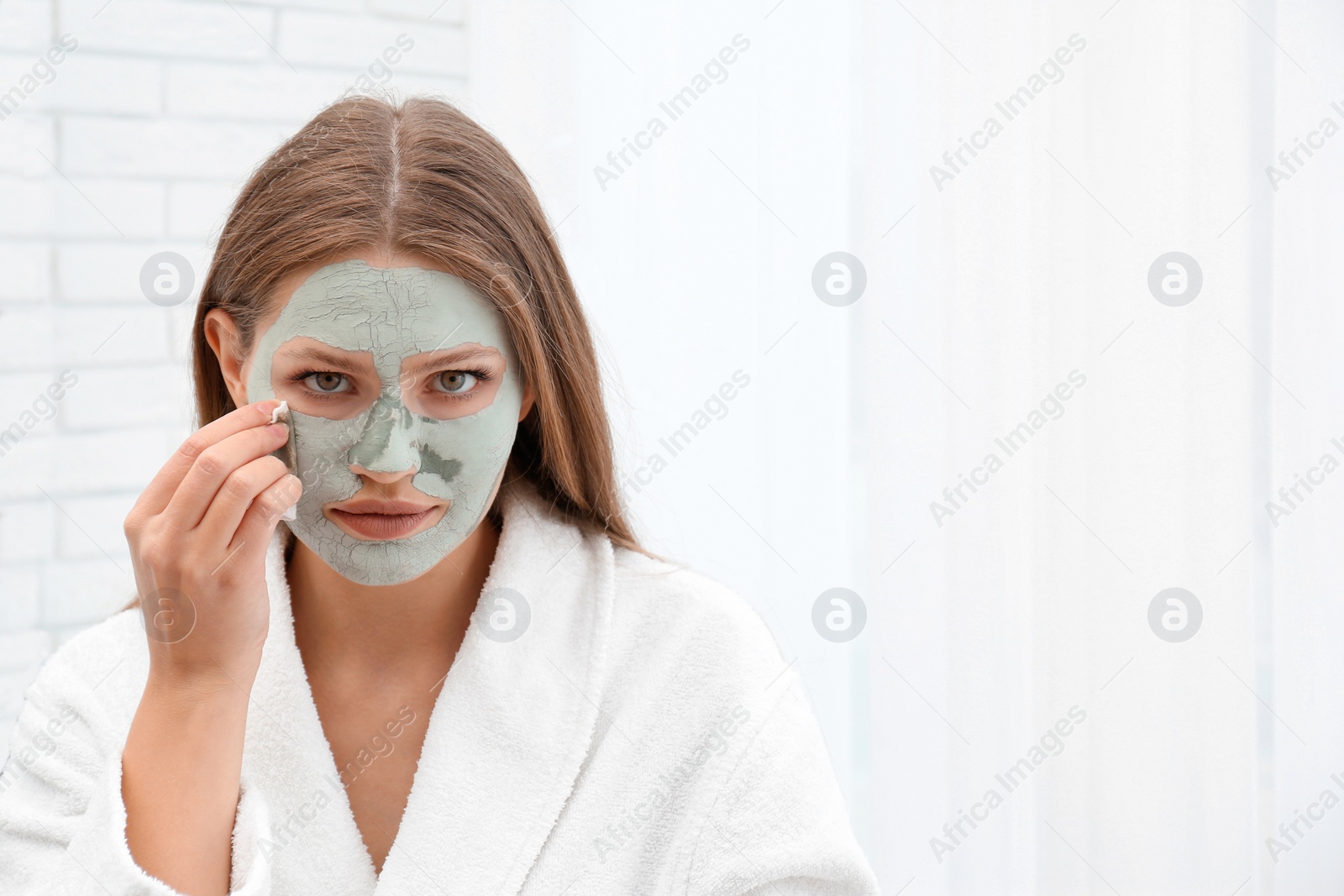 Photo of Beautiful woman removing clay mask from her face indoors