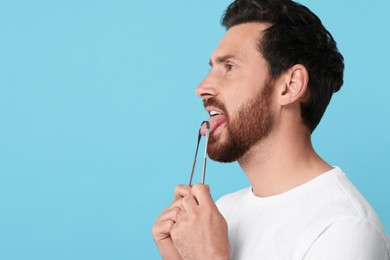 Photo of Handsome man brushing his tongue with cleaner on light blue background, space for text
