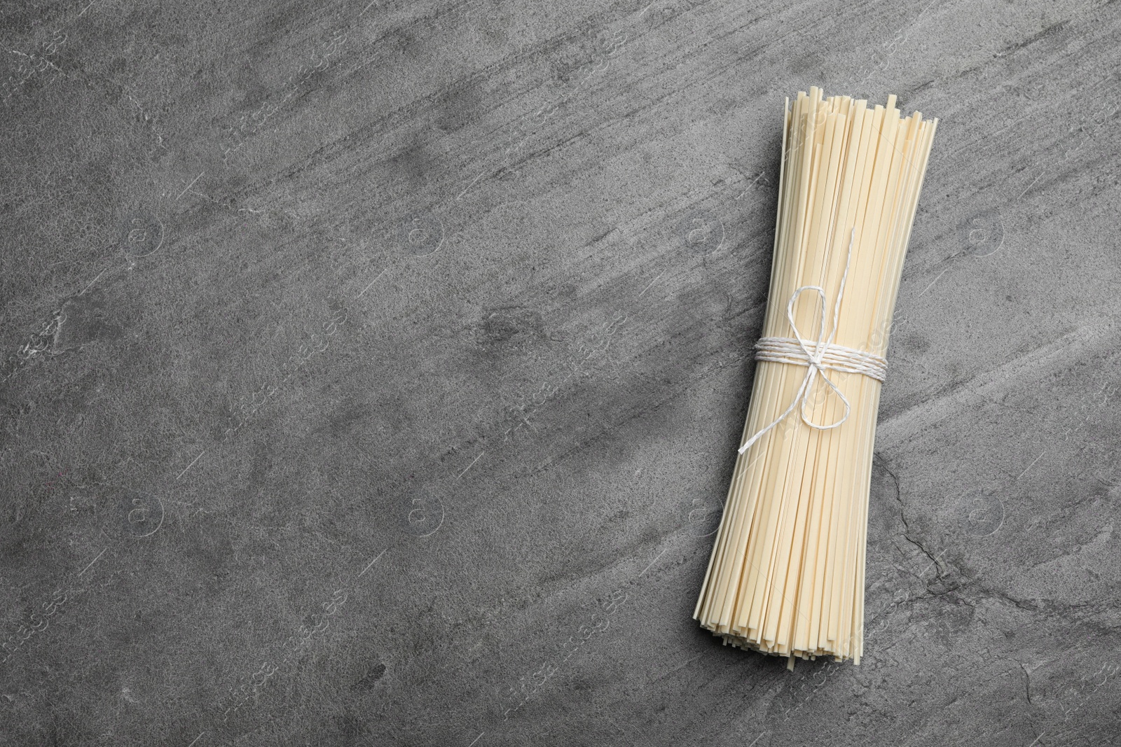 Photo of Raw rice noodles on grey table, top view. Space for text