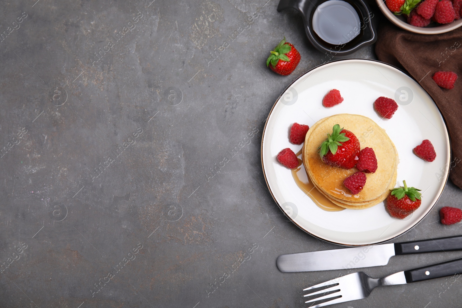 Photo of Tasty pancakes served with fresh berries and honey on grey table, flat lay. Space for text