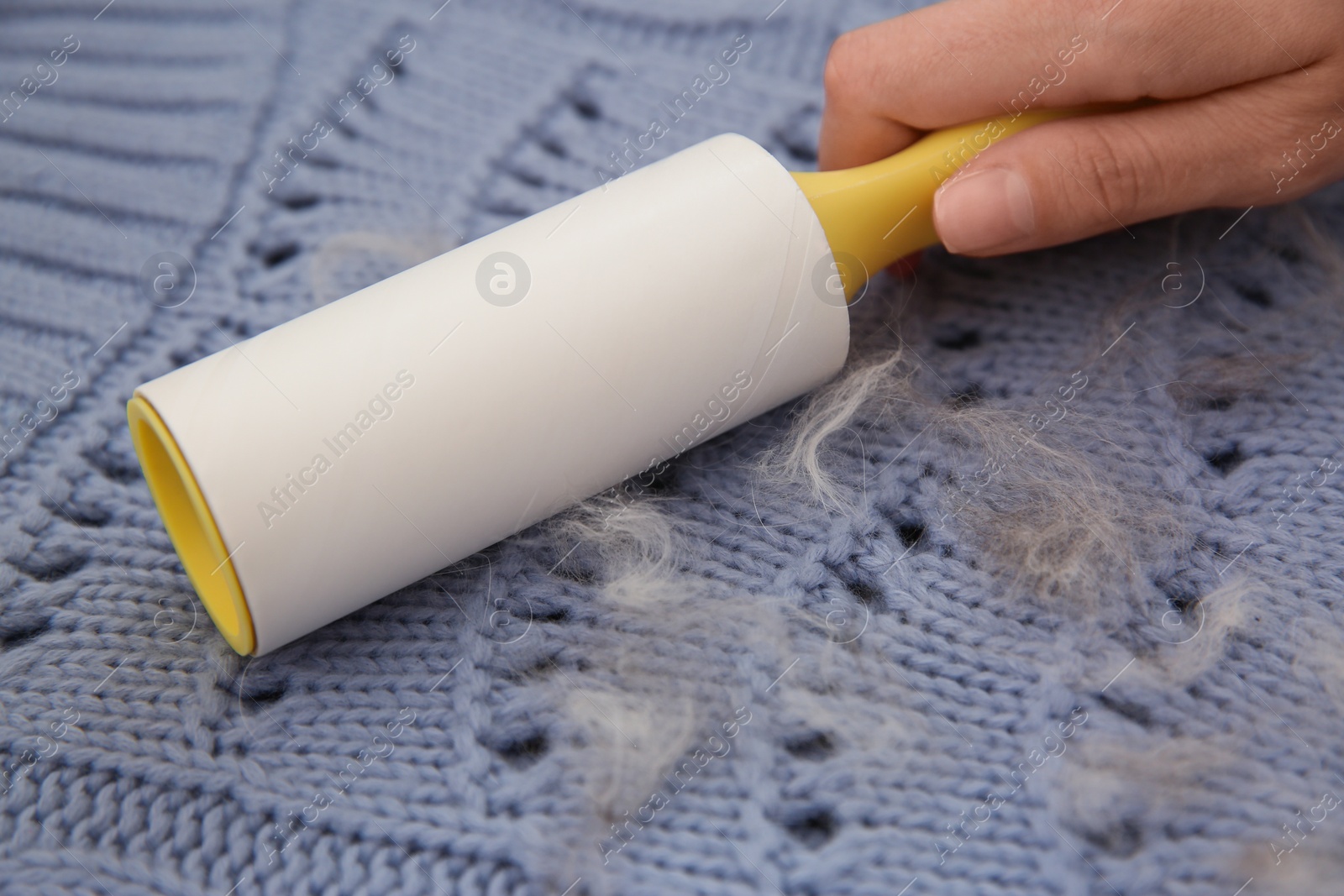 Photo of Woman removing hair from light blue knitted sweater with lint roller, closeup