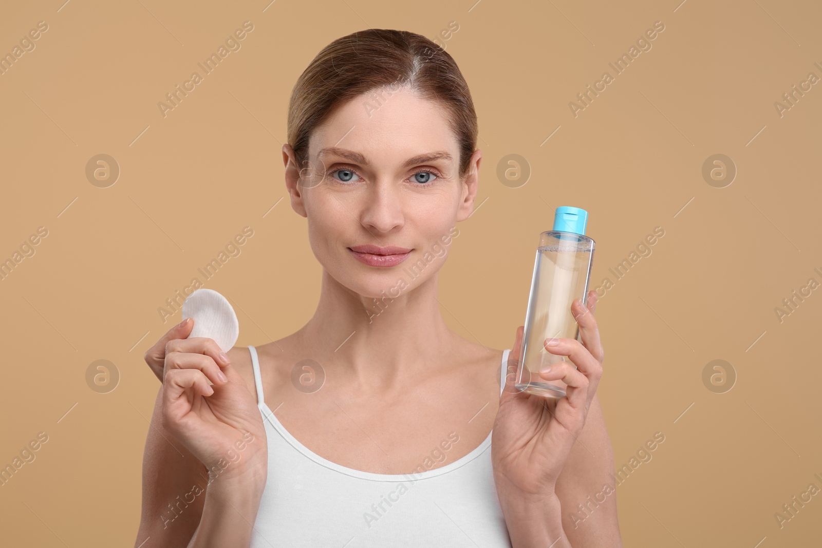 Photo of Beautiful woman with makeup remover and cotton pad on beige background