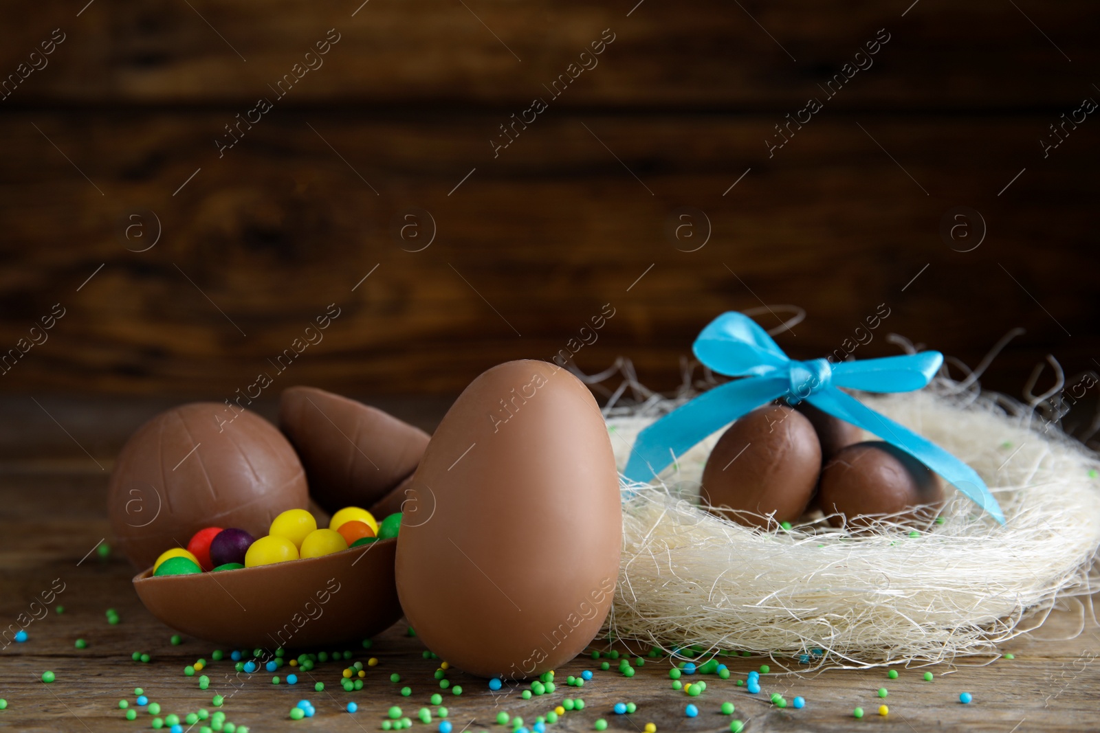 Photo of Composition with tasty chocolate eggs, colorful candies and decorative nest on wooden table, space for text