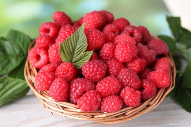 Photo of Tasty ripe raspberries and green leaves on light table, closeup