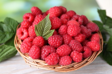 Tasty ripe raspberries and green leaves on light table, closeup