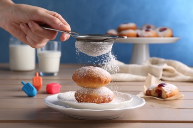 Photo of Woman dusting powdered sugar onto delicious Hanukkah donuts on wooden table, closeup
