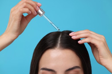 Woman applying hair serum on light blue background, closeup. Cosmetic product