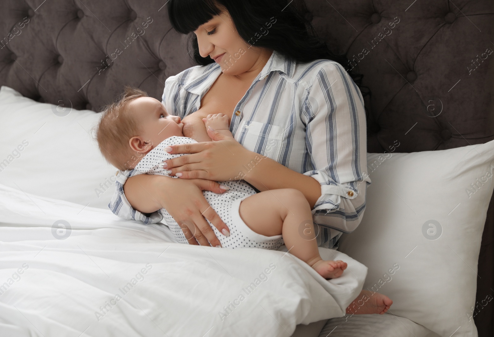 Photo of Woman breastfeeding her little baby on bed indoors