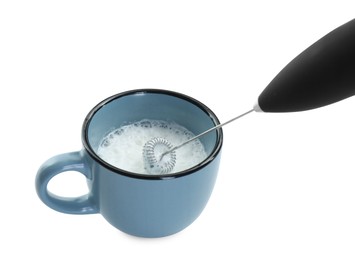 Photo of Whisking milk in cup with mini mixer (frother wand) isolated on white, closeup