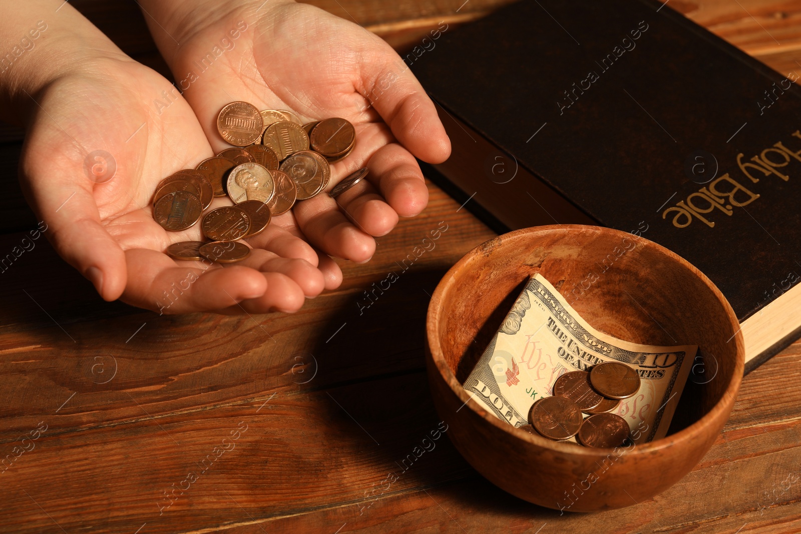 Photo of Donate and give concept. Woman holding coins, closeup. Bible and bowl of money on wooden table