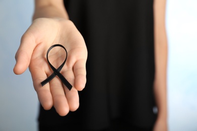 Photo of Woman holding black ribbon on light background, closeup. Funeral symbol