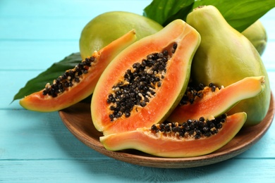 Photo of Fresh ripe papaya fruits with green leaves on turquoise wooden table, closeup