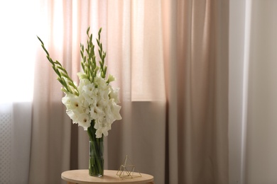 Vase with beautiful white gladiolus flowers on wooden table in room, space for text