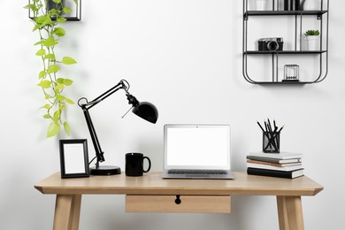 Photo of Cozy workspace with laptop, lamp and stationery on wooden desk at home
